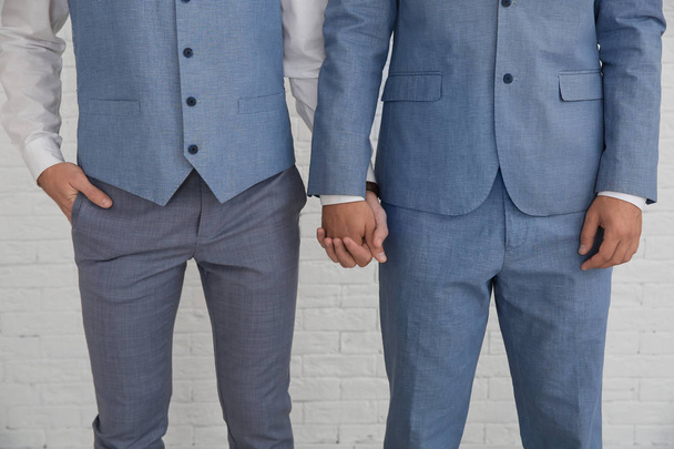 Newlywed gay couple holding hands near white wall, closeup - Foto, imagen