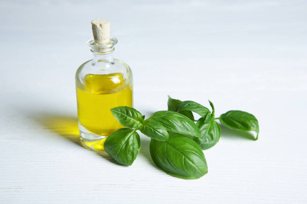 Glass bottle with oil and basil leaves on light table - Foto, afbeelding