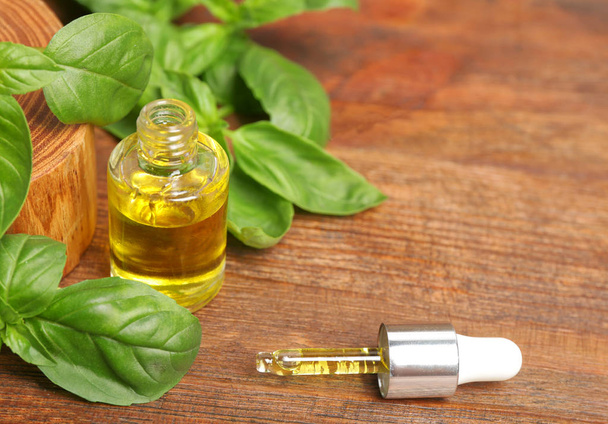 Glass bottle of oil with basil leaves and space for text on wooden table - Photo, Image
