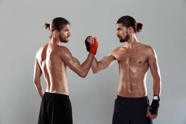 Portrait of a two confident muscular shirtless twin brothers standing isolated over gray background, boxing together, shaking hands - Fotoğraf, Görsel