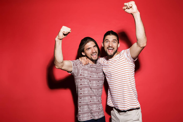 Portrait of a two young excited twin brothers isolated over red background, celebrating success - Fotó, kép