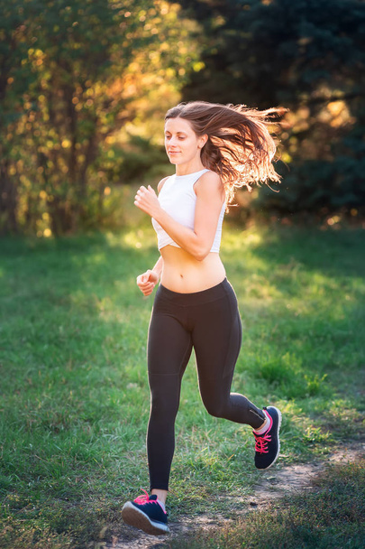 Beautiful young sportive woman jogging in the park in sunset light - Photo, Image