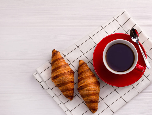 Croissantje en kopje koffie op een witte houten tafel. - Foto, afbeelding