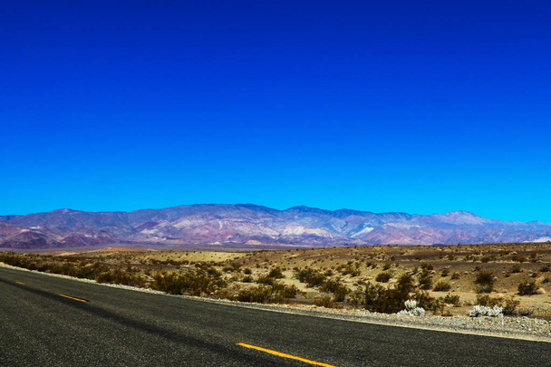 Klassischer vertikaler Rundblick auf eine endlos gerade Straße, die durch die karge Landschaft des amerikanischen Südwestens führt, mit extremem Hitzedunst an einem schönen heißen, sonnigen Tag mit blauem Himmel im Sommer. - Foto, Bild