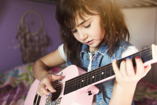 Little attractive girl with his guitar on his knees on the bed in the room - 写真・画像
