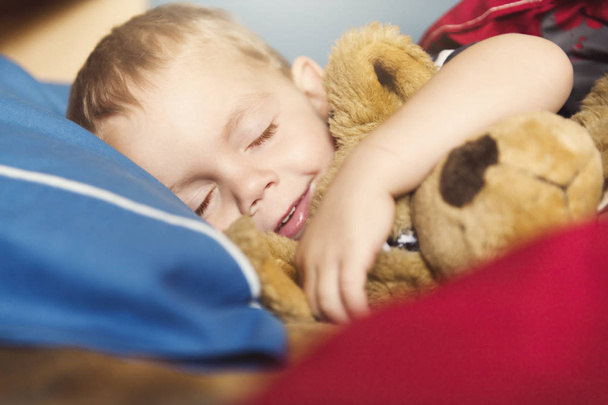 Child sleeping in his bed with teddy - Фото, изображение