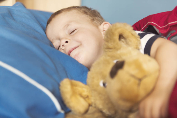 Child sleeping in his bed with teddy - 写真・画像
