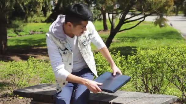 Man freelancer comes to park and start working on laptop - Кадры, видео