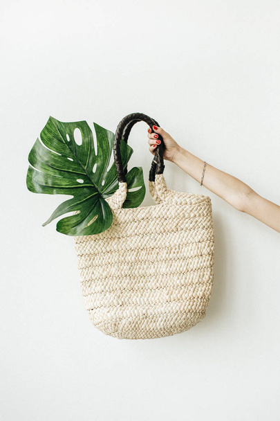 Female hand holding straw bag with monstera leaf on white background. - Photo, Image