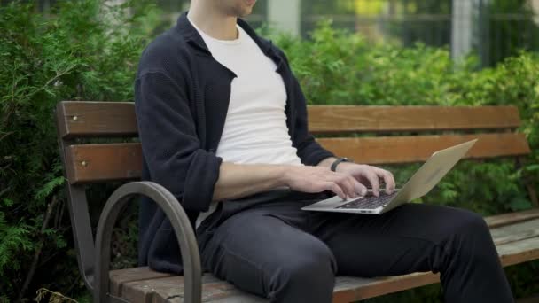 Unrecognizable man typing on laptop sitting on bench - 映像、動画