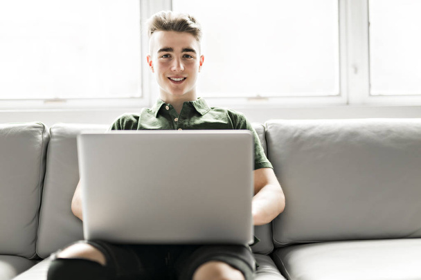 Handsome man using a laptop sitting on couch at home - Photo, image