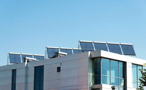 Вакуумная солнечная батарея для нагрева воды на современной крыше здания. Зеленая энергия, альтернативное отопление и системы энергоснабжения. Экологически чистая энергия солнечного света
 - Фото, изображение