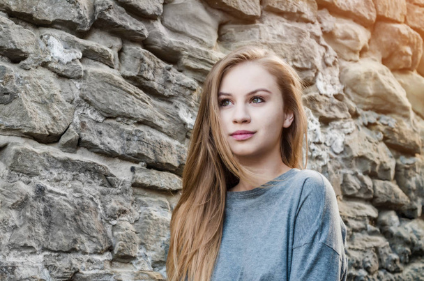Attractive girl with long blond hair is looking to the left against a wall of stone background. Youth sexuality. Fashionable girl. PHOTO on a journey. Tourism in Europe. - Photo, image