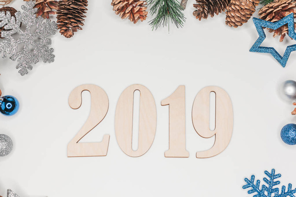 Christmas and New Year composition. 2019 simbols and fir branches with cones and christmas balls in silver and blue colours on white background. Flat lay, top view, copy space for text - Foto, afbeelding