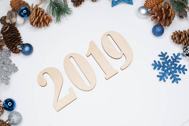 Christmas and New Year composition. 2019 simbols and fir branches with cones and christmas balls in silver and blue colours on white background. Flat lay, top view, copy space for text - Photo, image