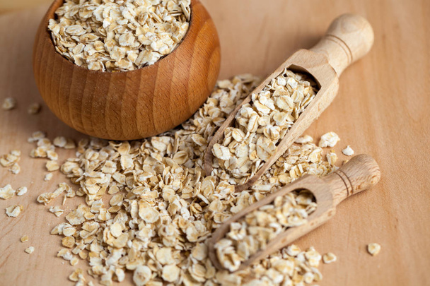 Oat flakes in a wooden bowl with a scoop on the wooden board. - Photo, Image