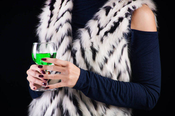 Mulher glamourosa com Absinthe bebida verde em vidro e colete de pele branca com padrão preto, fundo preto e escuro. Imagem de conceito de bebida e moda exótica
 - Foto, Imagem