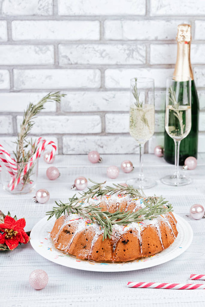 traditionelle Weihnachtsfruchtkuchen auf einem weißen Holztisch. hausgemachter Pudding mit festlicher Dekoration, Zuckerstangen und Champagnergläsern - Foto, Bild