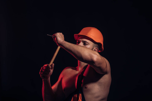 Site is under construction. Man work with hammer. Muscular man builder at work under construction. Hard worker use muscular strength. Construction worker hammer a nail - Foto, Bild