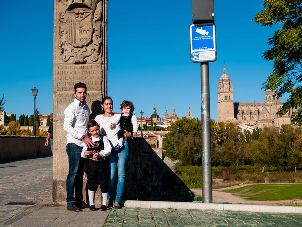 Una familia viajando con dos hermanos niños abrazados en el puente romano de Salamanca, vestidos con ropa tradicional y la catedral de Salamanca
 - Foto, imagen