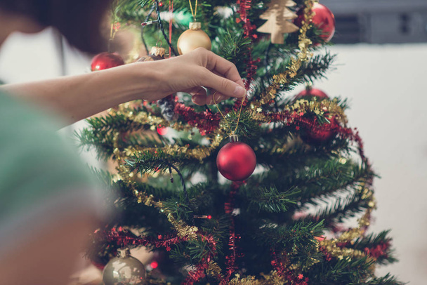 Retro-Bild einer Frau, die leuchtend rote Christbaumkugeln an den Weihnachtsbaum hängt. Blick über die Schulter. - Foto, Bild