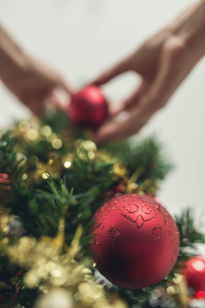 Low angle view of red holiday bauble hanging on Christmas tree with blurred female hands decorating the top part of the tree. With retro filter effect. - 写真・画像