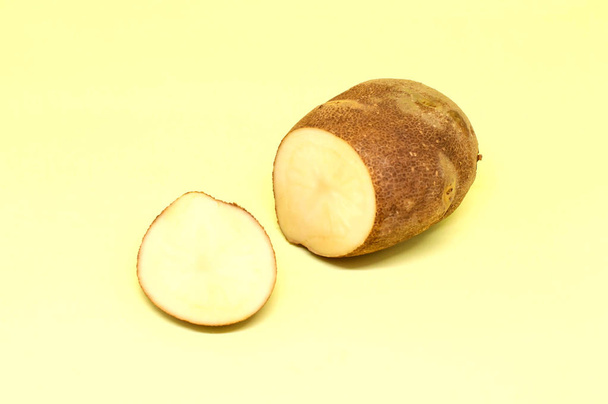 Сира необроблена картопля з вирізаним шматочком на світло-жовтому фоні
 - Фото, зображення