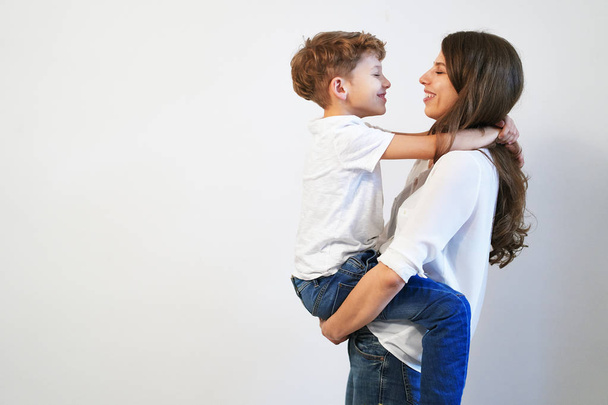 Young mother holding her preteen son smiling and looking into his eyes on white background with copy space - Photo, Image