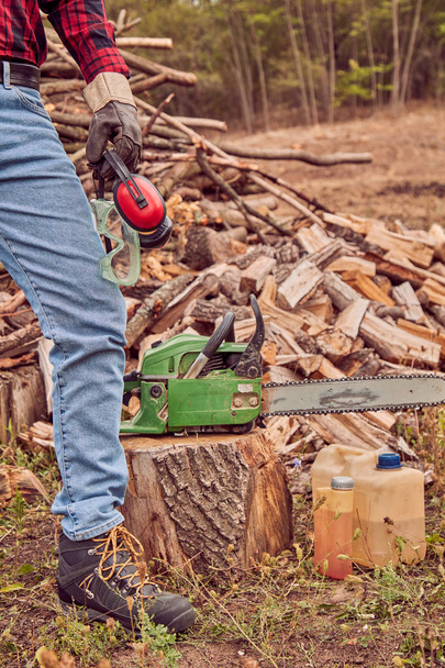 Lumberjack with chainsaw and pile of cut woods. - Photo, Image