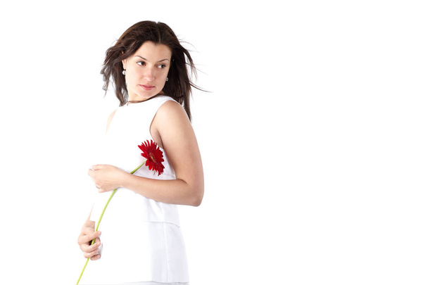 Gyönyörű fiatal nő fehér ruhában, pózol, piros gerbera portréja - Fotó, kép