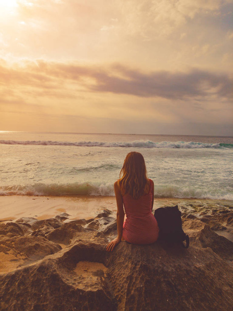 Chica sentada en una playa de arena y mirando el paisaje oceánico
. - Foto, imagen