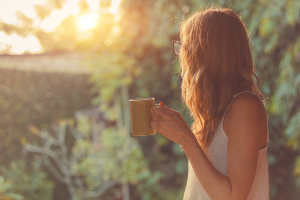 Милая девушка наслаждается утренним кофе на крыльце
. - Фото, изображение