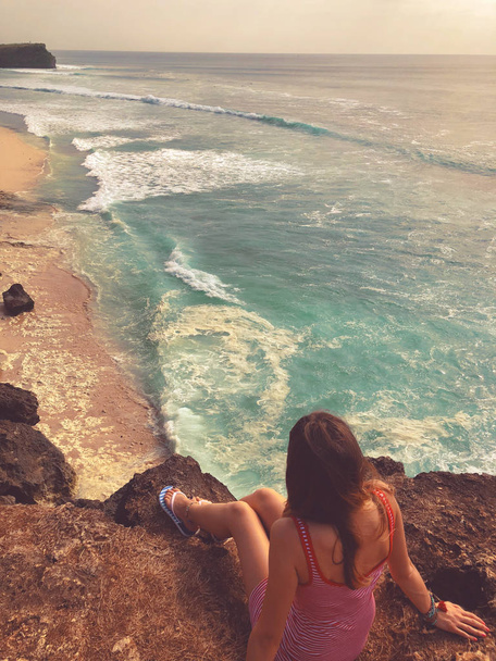 Yalnız kız okyanus üzerinde yüksek bir kayalığın üzerinde oturan. - Fotoğraf, Görsel