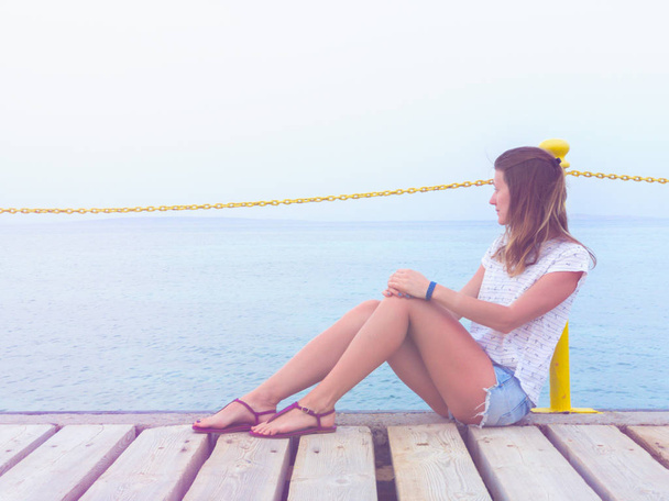 Dziewczyna siedzi na drewniane Kret / molo i patrząc na Oceanie. - Zdjęcie, obraz