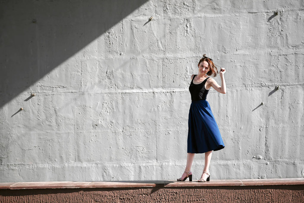 jovem posando contra uma parede de concreto, vestida de preto, luz dura e sombras
 - Foto, Imagem