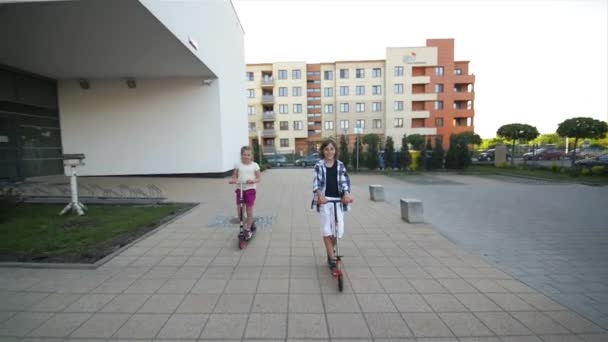 Chica y niño montando patada scooter al aire libre. Feliz lindo niños jugando en la calle aprender a equilibrar en patada tablero en el campo
. - Imágenes, Vídeo