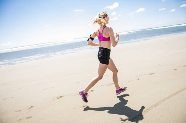Young woman jogging on the beach in summer day. Athlete runner exercising actively in sunny day - Fotó, kép
