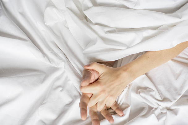 couples hold hands together in bed close-up touching each other on a white sheets. Couple having sex - Фото, зображення