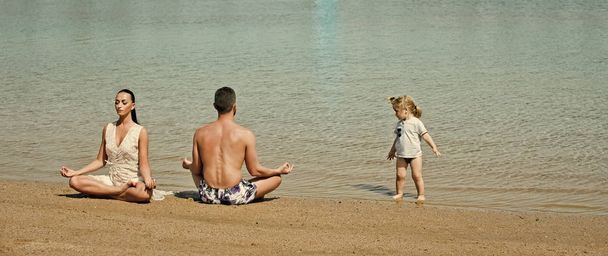 mother, father and child doing yoga exercises on beach, people outdoor, concept of friendly family and of summer vacation near water - Fotografie, Obrázek