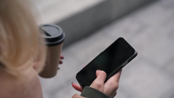 Hand of woman with coffee swiping across smartphone screen - Záběry, video