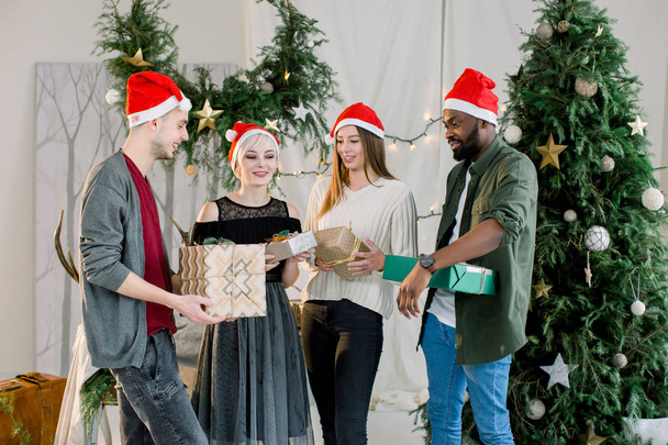 Happy three Caucasian women, Caucasian man and African man holding Christmas presents at home. Christmas tree. - Фото, зображення