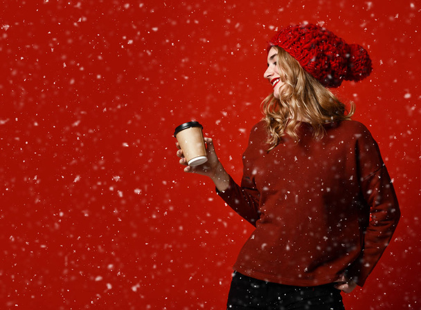 Pretty brunette woman in warm clothes drinking hot chocolate or coffee on red - Фото, зображення