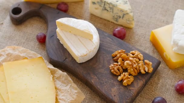 Cheese platter with nuts and grapes on a wooden cutting board - Footage, Video