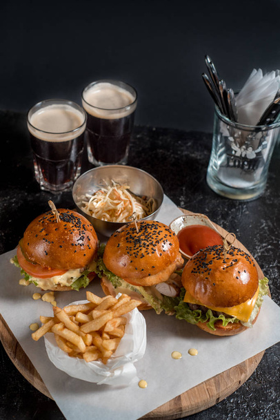 Set three burger, french fries, ketchup sauce, salad and two glasses of dark beer. Hearty set for Oktoberfest on a dark background copy space - Photo, Image