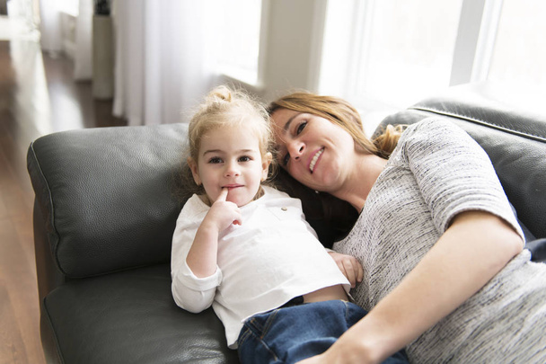 Happy mother with her daughter on the sofa in the living room at home - 写真・画像