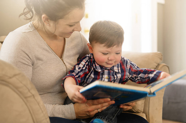 Mother reading book with her child on sofa - Фото, зображення
