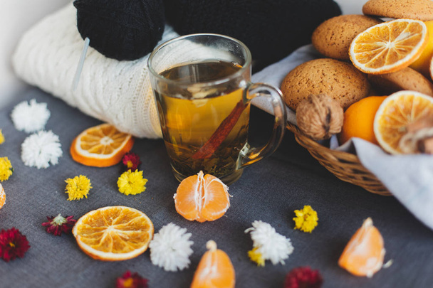 Tangerines, flowers, gingerbread, citrus in sraw basket, warm sweater, cup of tea and orange slices. Christmas winter background, wallpaper, greeting card. Top view, flat lay, background, copy spaces - Photo, Image
