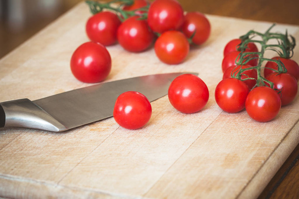 Tomates cherry (Solanum lycopersicum) y un cuchillo en una tabla de cortar de madera
 - Foto, imagen