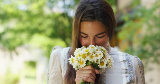 video of brunette woman smelling white daisies flowers bouquet and showing on camera  - Séquence, vidéo
