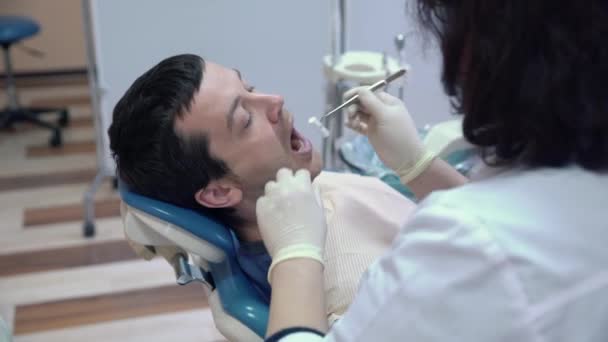 A dentist woman in a sterile mask and clothes performs procedures in the patients mouth with medical instruments. Dental treatment in a dental clinic. Health concept. - Filmati, video